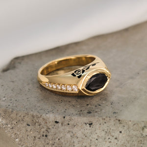 Close-up photo of a 14k Yellow Gold ring with a horizontal Marquise-cut 1ct black diamond center stone. The band features black enamel rose on one side and 3 black enamel hearts on the other, accentuated with VS diamonds pave set in the corners. The ring has a unique and distinctive design, perfect for any special occasion.