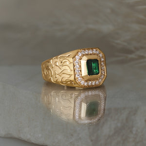 signet style 14k yellow gold ring with a green tourmaline square shape bezel set followed by a diamond halo with cut corners, engraved with waves on one side and fire on the other side.