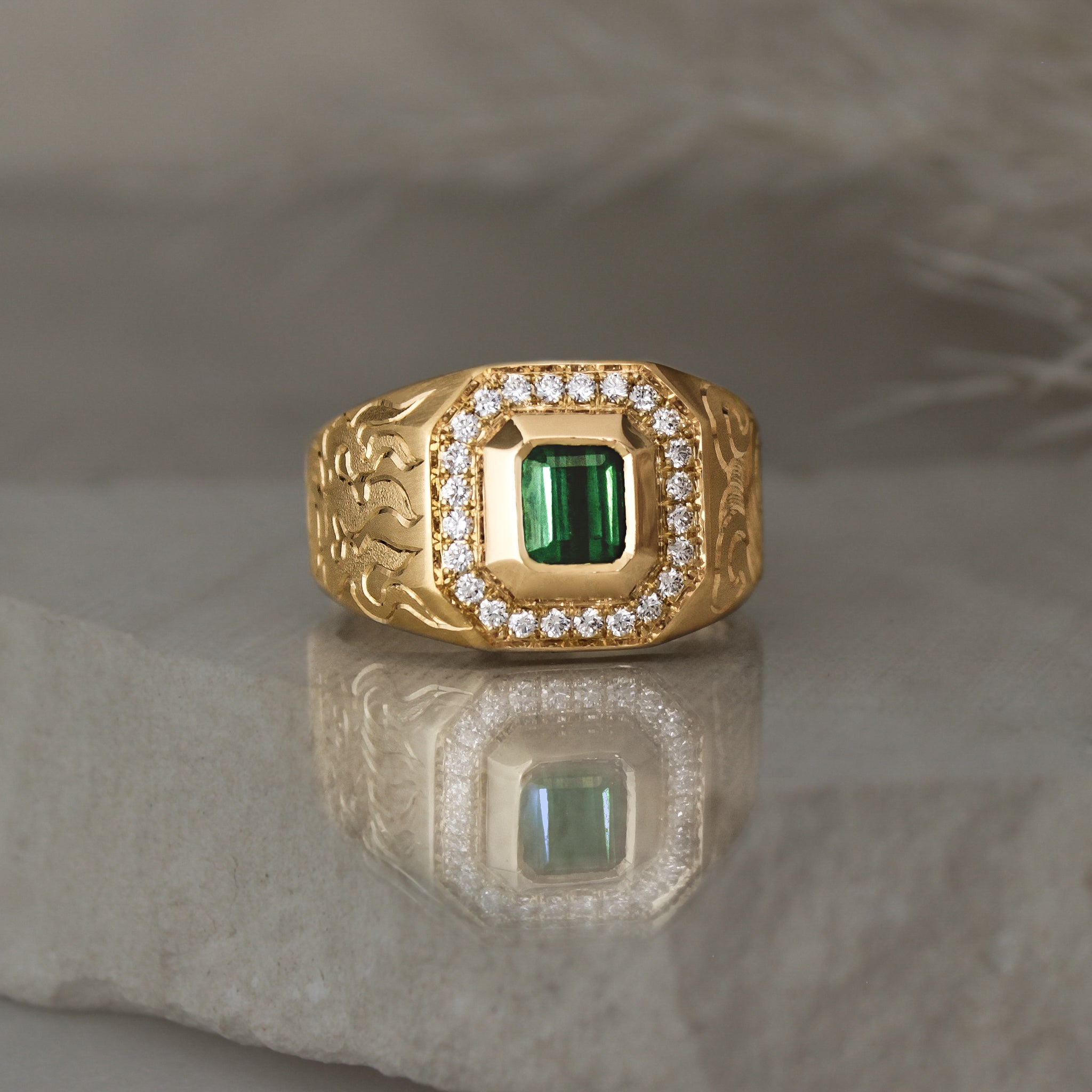 signet style 14k yellow gold ring with a green tourmaline square shape bezel set followed by a diamond halo with cut corners, engraved with waves on one side and fire on the other side.