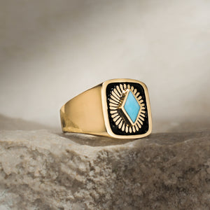 Close-up of a 14k Yellow Gold signet ring with black enamel background and turquoise bezel set hand engraved with a ray of sunshine pattern behind the stone